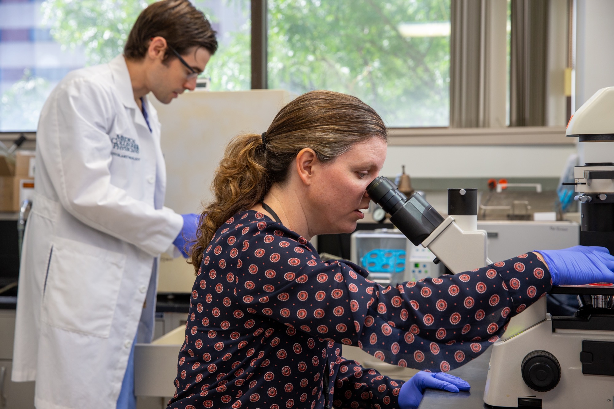 A researcher at a microscope while Joseph Zenga works in the laboratory background